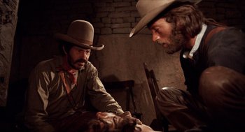 Movie still from “The Hired Hand” (1971), directed by Peter Fonda – Two men in cowboy hats are looking at a dead body; Medium shot, Over the shoulder angle