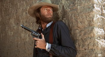 Movie still from “The Hired Hand” (1971), directed by Peter Fonda – A man with a beard and a cowboy hat holding a gun; Medium shot, Low angle