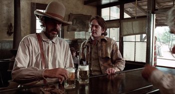 Movie still from “The Hired Hand” (1971), directed by Peter Fonda – Two men sitting at a table with a beer; Medium shot, Low angle