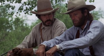 Movie still from “The Hired Hand” (1971), directed by Peter Fonda – A couple of men sitting next to each other on the ground; Medium shot, Low angle