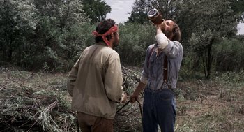 Movie still from “The Hired Hand” (1971), directed by Peter Fonda – Two men are standing in a field drinking from a bottle; Medium shot, Over the shoulder angle