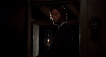 Movie still from “The Hired Hand” (1971), directed by Peter Fonda – A man standing in a dark room next to an oil lamp; Medium shot, Over the shoulder angle