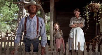 Movie still from “The Hired Hand” (1971), directed by Peter Fonda – A man and a woman and a little girl standing in front of a wooden fence; Medium shot, Low angle