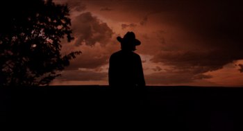Movie still from “The Hired Hand” (1971), directed by Peter Fonda – A man wearing a cowboy hat standing in front of a sunset; Wide shot, Low angle