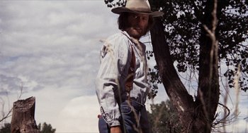 Movie still from “The Hired Hand” (1971), directed by Peter Fonda – A man wearing a cowboy hat standing next to a tree; Medium shot, Low angle