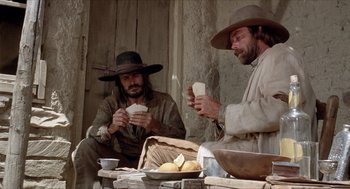 Movie still from “The Hired Hand” (1971), directed by Peter Fonda – Two men sitting on a bench eating food; Medium shot, Low angle