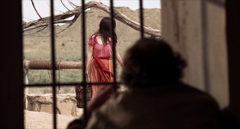 Movie still from “The Hired Hand” (1971), directed by Peter Fonda – A woman in a red and pink dress standing in front of a tree; Wide shot, Over the shoulder angle