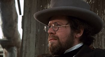 Movie still from “The Hired Hand” (1971), directed by Peter Fonda – A man with a beard wearing glasses and a hat; Close Up shot, Over the shoulder angle