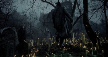 A man walking through a graveyard with candles in front of him