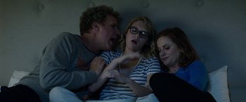 Movie still from “The House” (2017), directed by Andrew Jay Cohen – Two women and a man are sitting in a bed together; Medium shot, Over the shoulder angle