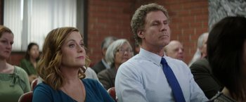 Movie still from “The House” (2017), directed by Andrew Jay Cohen – A man and a woman sitting next to each other in front of a brick wall; Medium shot, Over the shoulder angle