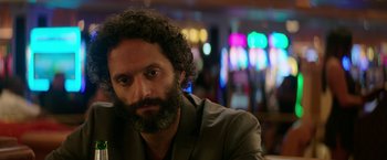 Movie still from “The House” (2017), directed by Andrew Jay Cohen – A man with curly hair and a beard sitting at a table; Close Up shot, Over the shoulder angle