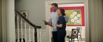 Movie still from “The House” (2017), directed by Andrew Jay Cohen – A man and a woman standing next to each other holding a tablet; Medium shot, Over the shoulder angle