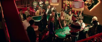 Movie still from “The House” (2017), directed by Andrew Jay Cohen – A group of people standing around a table with cards; Wide shot, High angle