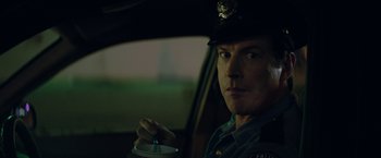 Movie still from “The House” (2017), directed by Andrew Jay Cohen – A police officer sitting in the drivers seat of a car; Close Up shot, Over the shoulder angle