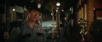 Movie still from “The House” (2017), directed by Andrew Jay Cohen – A man in a police uniform standing in the street; Close Up shot, Over the shoulder angle