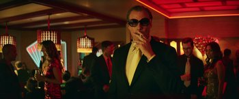 Movie still from “The House” (2017), directed by Andrew Jay Cohen – A man in a suit and sunglasses smoking a cigarette; Medium shot, Low angle