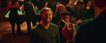 Movie still from “The House” (2017), directed by Andrew Jay Cohen – A man smiles at the camera while a woman takes a picture; Medium shot, Over the shoulder angle