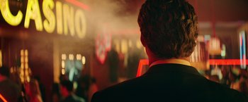 Movie still from “The House” (2017), directed by Andrew Jay Cohen – A man in a black suit standing in front of a neon sign; Close Up shot, Over the shoulder angle