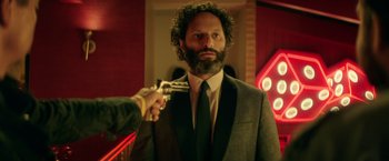 Movie still from “The House” (2017), directed by Andrew Jay Cohen – A man in a suit holding a gun pointed at him; Close Up shot, Over the shoulder angle