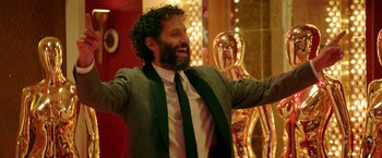 Movie still from “The House” (2017), directed by Andrew Jay Cohen – A man in a suit and tie holding a trophy; Medium shot, Low angle