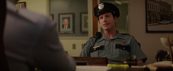 Movie still from “The House” (2017), directed by Andrew Jay Cohen – A police officer sitting at a table with a cat; Medium shot, Over the shoulder angle