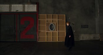 Movie still from “The Human Voice” (2020), directed by Pedro Almodóvar – A woman in a black coat walking in front of a wall; Wide shot, Over the shoulder angle