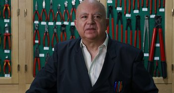 Movie still from “The Human Voice” (2020), directed by Pedro Almodóvar – An older man in a suit standing in front of a wall of pliers; Close Up shot, Low angle