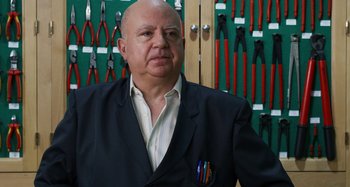 Movie still from “The Human Voice” (2020), directed by Pedro Almodóvar – A bald man in a suit stands in front of a wall of pliers; Close Up shot, Over the shoulder angle