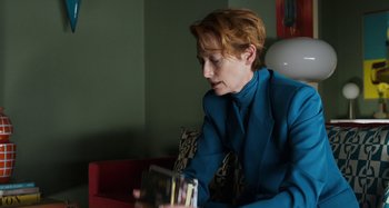 Movie still from “The Human Voice” (2020), directed by Pedro Almodóvar – A woman sitting on a couch looking at a book; Medium shot, Over the shoulder angle