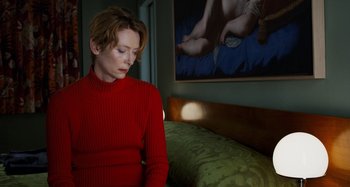 Movie still from “The Human Voice” (2020), directed by Pedro Almodóvar – A woman in a red sweater sitting in front of a painting; Medium shot, Low angle