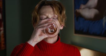 Movie still from “The Human Voice” (2020), directed by Pedro Almodóvar – A woman in a red sweater drinking from a glass; Close Up shot, High angle