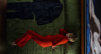 Movie still from “The Human Voice” (2020), directed by Pedro Almodóvar – A woman in a red outfit laying on a bed next to clothes; Wide shot, Overhead angle
