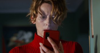 Movie still from “The Human Voice” (2020), directed by Pedro Almodóvar – A woman in a red sweater looking at a cell phone; Close Up shot, Low angle