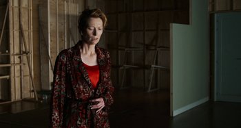 Movie still from “The Human Voice” (2020), directed by Pedro Almodóvar – An older woman wearing a red shirt and a red robe; Medium shot, Low angle