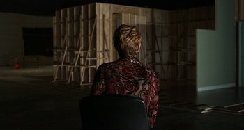 Movie still from “The Human Voice” (2020), directed by Pedro Almodóvar – A woman sitting in a chair in front of a wooden structure; Wide shot, Over the shoulder angle