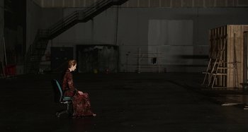 Movie still from “The Human Voice” (2020), directed by Pedro Almodóvar – A woman sitting on top of a chair in an empty parking lot; Wide shot, High angle