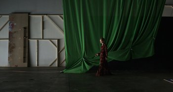 Movie still from “The Human Voice” (2020), directed by Pedro Almodóvar – A woman in a red dress standing in front of a green curtain; Wide shot, High angle