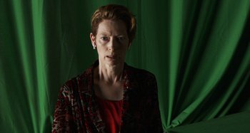 Movie still from “The Human Voice” (2020), directed by Pedro Almodóvar – A woman in a red shirt and a green curtain; Medium shot, Low angle