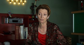 Movie still from “The Human Voice” (2020), directed by Pedro Almodóvar – A woman in a red shirt is sitting in front of a book shelf; Close Up shot, Over the shoulder angle