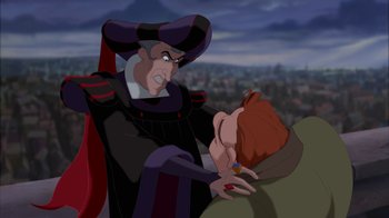 Movie still from “The Hunchback of Notre Dame” (1996), directed by Gary Trousdale – A man in a hat is holding another man's face; Medium shot, Over the shoulder angle