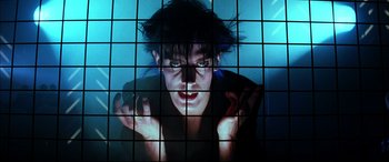 Movie still from “The Hunger” (1983), directed by Tony Scott – A man with blue hair is looking at the camera through a window pane; Close Up shot, Low angle