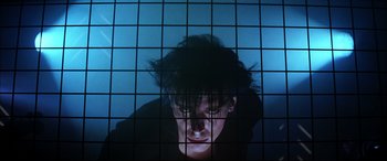 Movie still from “The Hunger” (1983), directed by Tony Scott – A man with long black hair is looking through a window; Close Up shot, Low angle