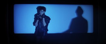 Movie still from “The Hunger” (1983), directed by Tony Scott – A woman in a black leather jacket is smoking a cigarette; Medium shot, Low angle