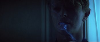 Movie still from “The Hunger” (1983), directed by Tony Scott – A man smoking a cigarette in a dark room; Close Up shot, Overhead angle