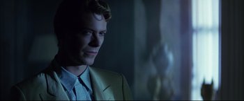 Movie still from “The Hunger” (1983), directed by Tony Scott – A man in a suit and tie looking at the camera; Close Up shot, Over the shoulder angle