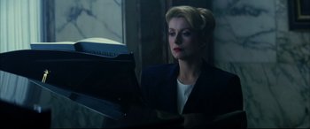 Movie still from “The Hunger” (1983), directed by Tony Scott – A woman in a suit looking at something on a book; Medium shot, Low angle