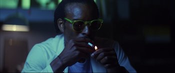 Movie still from “The Hunger” (1983), directed by Tony Scott – A man with glasses is lighting a cigarette; Close Up shot, Low angle