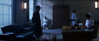 Movie still from “The Hunger” (1983), directed by Tony Scott – A man wearing a hat and a black suit standing next to a woman; Wide shot, Over the shoulder angle