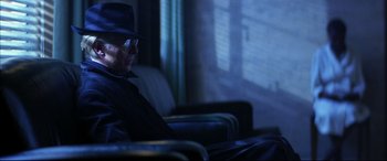 Movie still from “The Hunger” (1983), directed by Tony Scott – A man sitting in a chair wearing a hat and sunglasses; Medium shot, Low angle